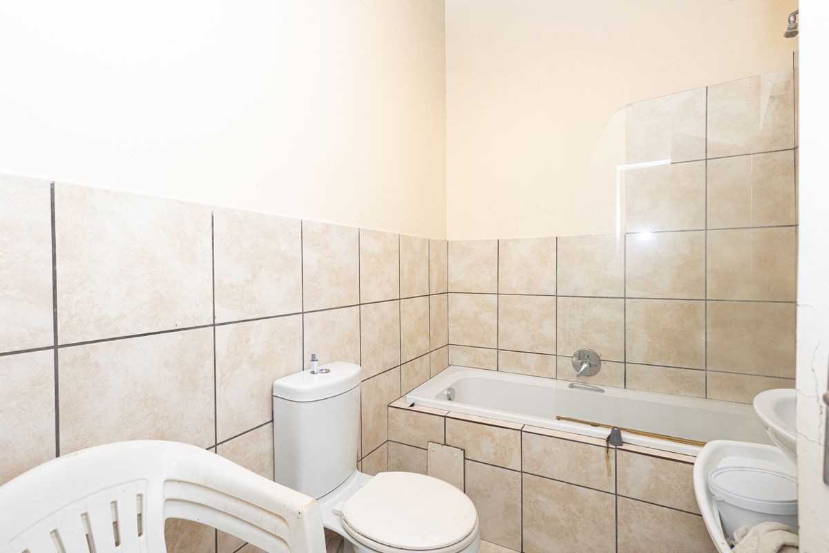 A functional bathroom featuring a built-in bathtub with a glass screen, a toilet, and a wall-mounted basin with neutral ceramic wall tiling.