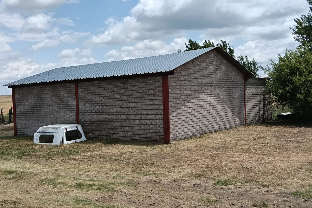 A view of a brick-constructed farm outbuilding featuring a corrugated metal roof and steel structural supports.