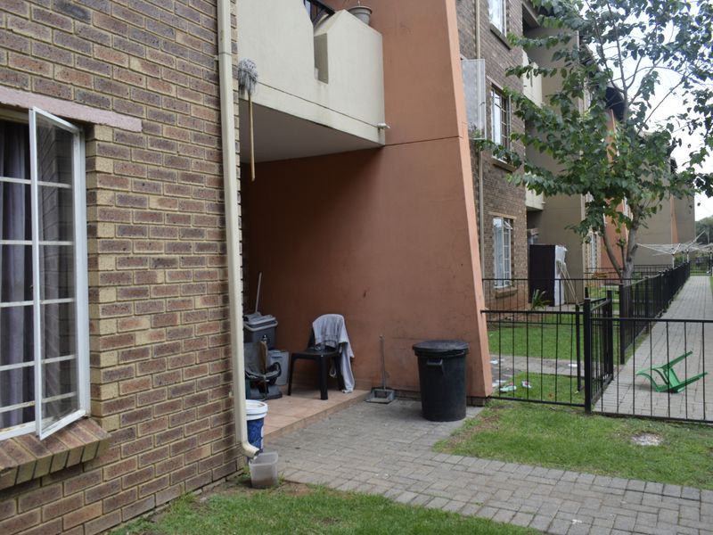 Rear view of the townhouse featuring a brick facade, a small paved patio area, and metal perimeter fencing leading to a communal garden space.