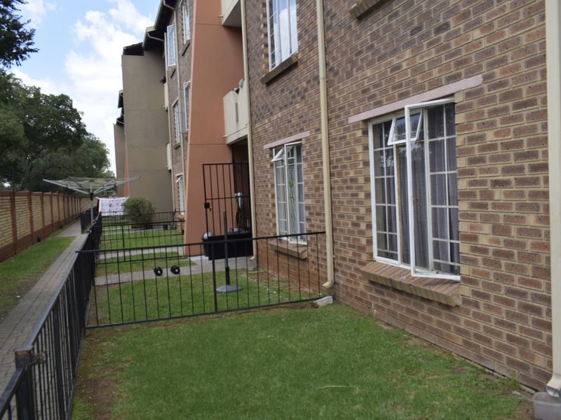 Rear exterior view of a townhouse complex featuring face brick facade, small private garden areas with metal fencing, and paved walkways.