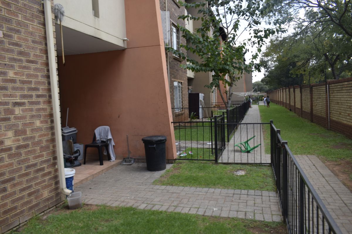 Rear exterior view of the townhouse featuring a paved patio area, metal fencing, and a shared garden walkway along the boundary wall.