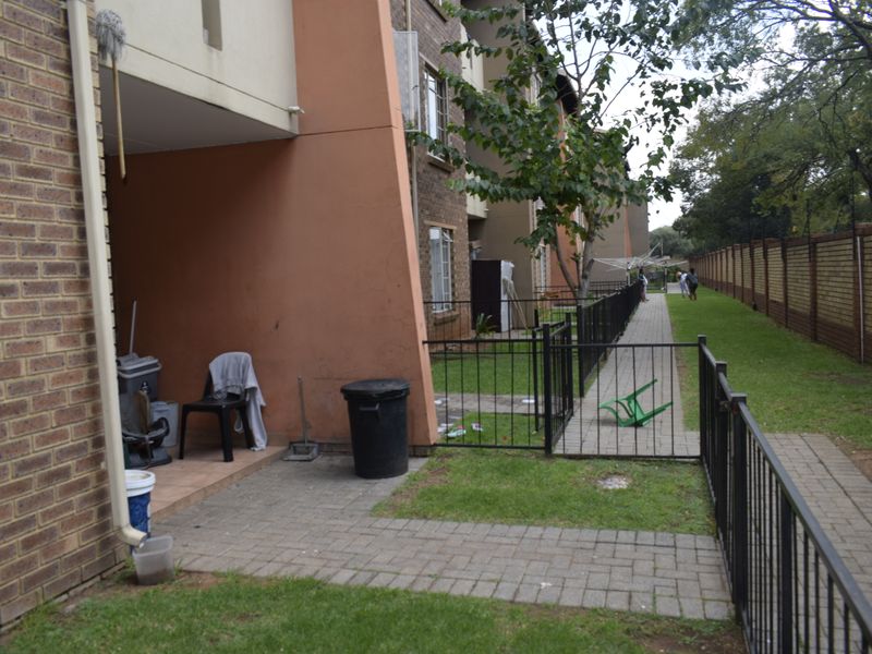 Rear exterior view of the townhouse featuring a paved patio area, metal fencing, and a shared garden walkway along the boundary wall.