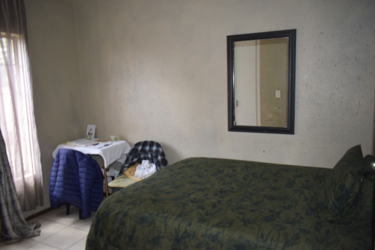 A bedroom featuring tiled flooring and a window with curtains, requiring cosmetic updates to the wall finishes to improve the overall aesthetic.