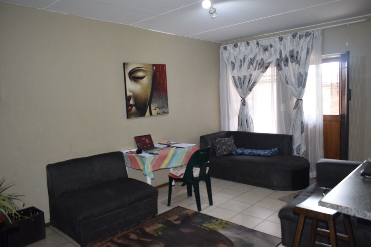 A functional living room area featuring tiled flooring and natural light access through a window with curtain rails.