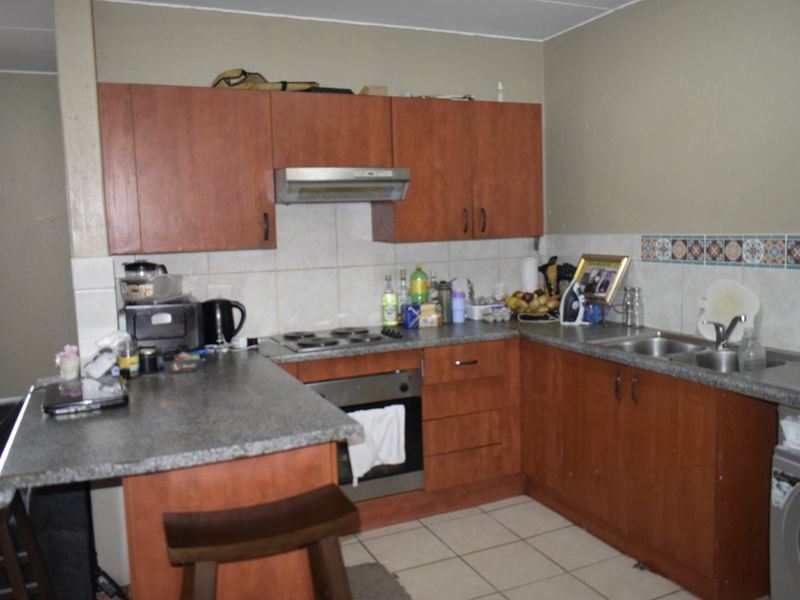 Functional kitchen featuring wood-look cabinetry, granite-style countertops, built-in oven and hob, and a double stainless steel sink with tiled splashback.
