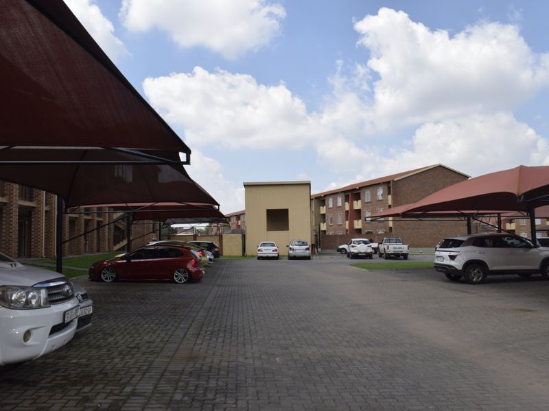 Exterior view of the townhouse complex featuring a paved parking area with installed shade cloth carports and brick building facades.