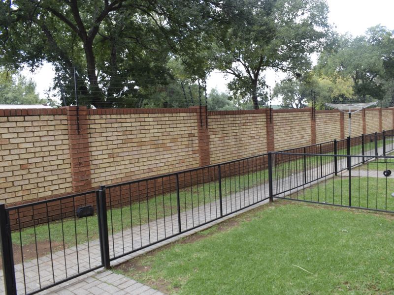 A private rear garden area featuring a secure brick boundary wall with electric fencing, a paved walkway, and a well-maintained lawn.