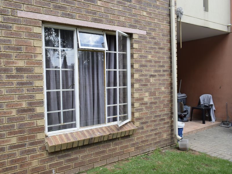 Rear exterior view of the townhouse featuring a brick facade, a casement window, and a small paved patio area.