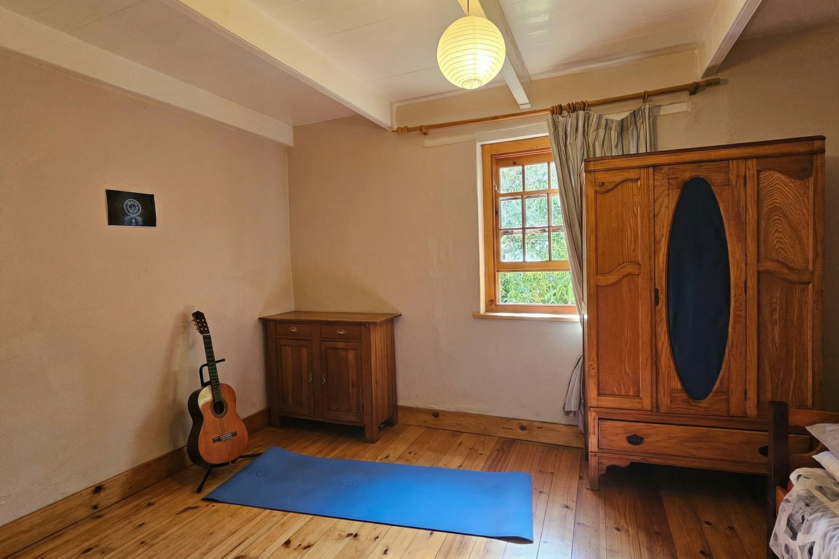 A bedroom featuring exposed timber ceiling beams, natural wood flooring, and a timber-framed window providing natural light.