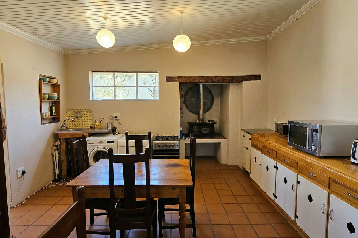A rustic kitchen featuring wooden cabinetry, a built-in stove area, tiled flooring, and a dedicated laundry space with a washing machine connection.