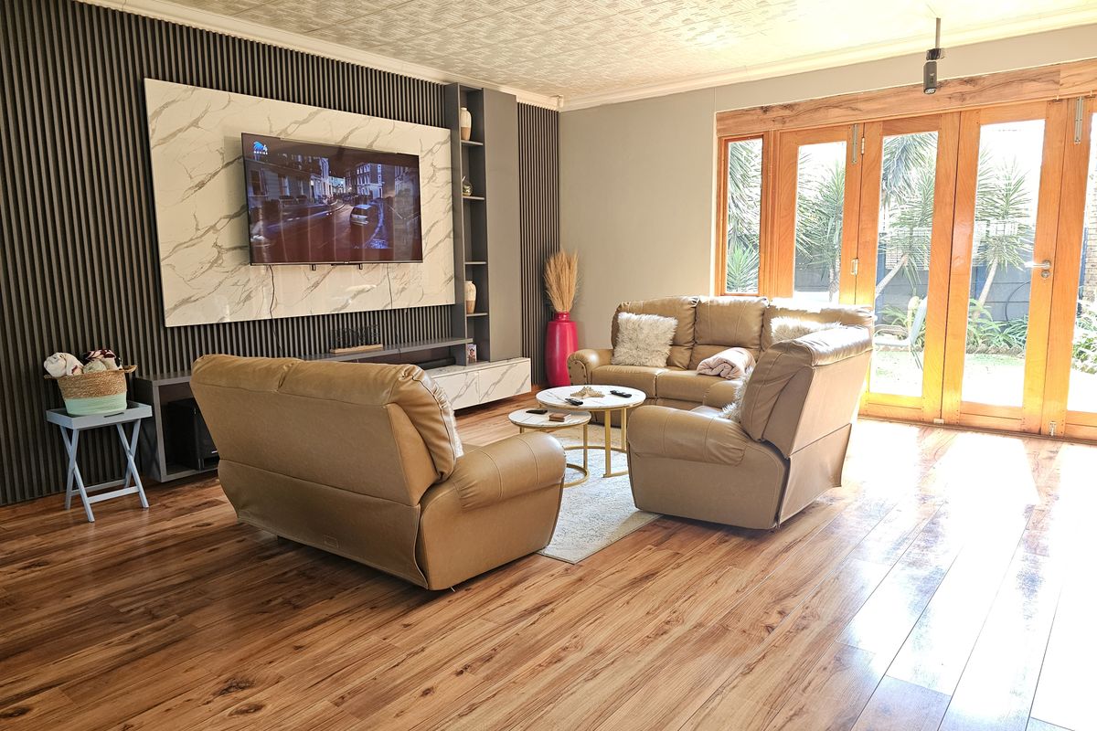 A well-maintained living room featuring laminate flooring, a modern slatted feature wall with marble-look paneling, and timber-framed glass doors opening to the garden.