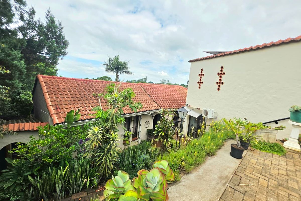 A view of the rear exterior featuring a terracotta tiled roof, paved patio area, and established garden landscaping.
