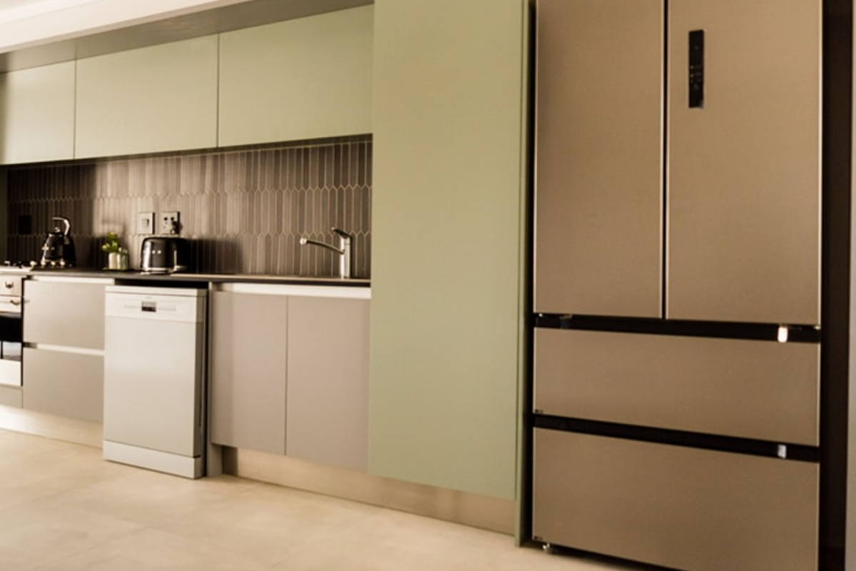 Modern kitchen featuring sage green cabinetry, dark tiled backsplash, integrated oven, and sleek stainless steel appliances.