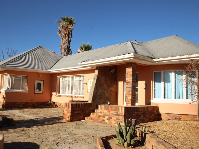 Front elevation of a single-story house featuring a corrugated metal roof, brick and stone facade, and a paved entrance patio.