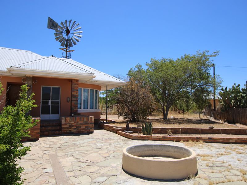 Rear exterior view featuring a stone patio, brick retaining walls, a concrete water feature, and a traditional windmill set against a rural landscape.