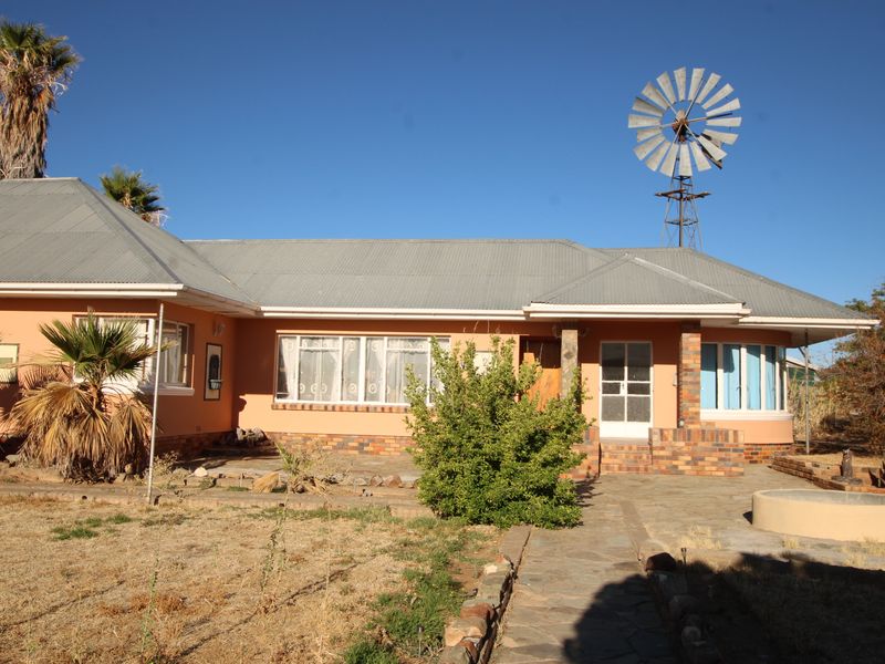Front view of a single-story house featuring a corrugated metal roof, brick accents, a stone walkway, and a traditional windmill in the yard.