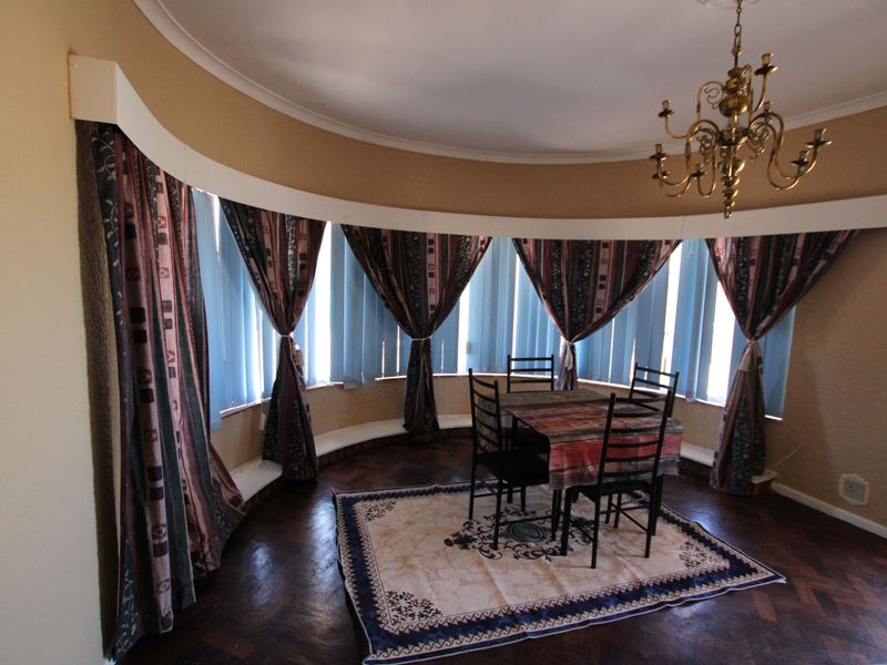 A dining room featuring a distinctive curved bay window, classic parquet flooring, and a traditional brass chandelier, offering a unique architectural layout.
