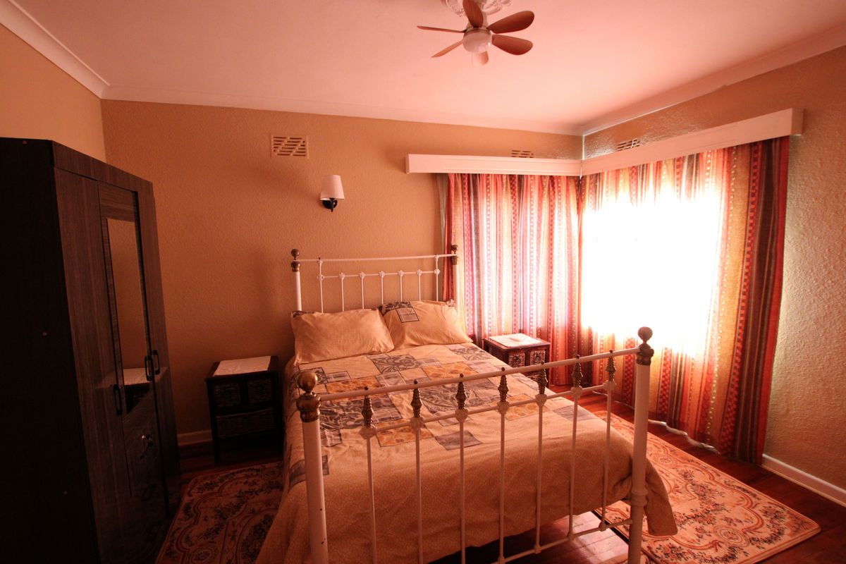 A bedroom featuring hardwood flooring, a ceiling fan, and wall-mounted lighting, with natural light entering through large windows.