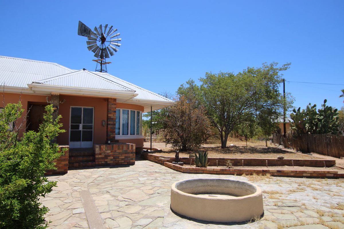 Rear exterior view featuring a stone patio, brick retaining walls, a concrete water feature, and a traditional windmill set against a rural landscape.