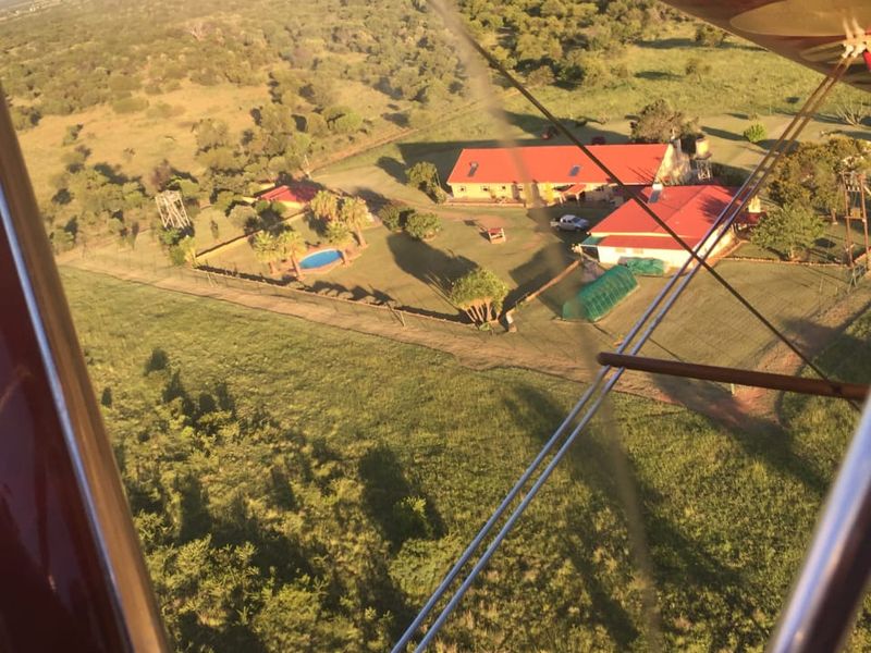 Aerial view of the small holding property featuring multiple buildings with red metal roofs, a swimming pool, and surrounding landscaped grounds.