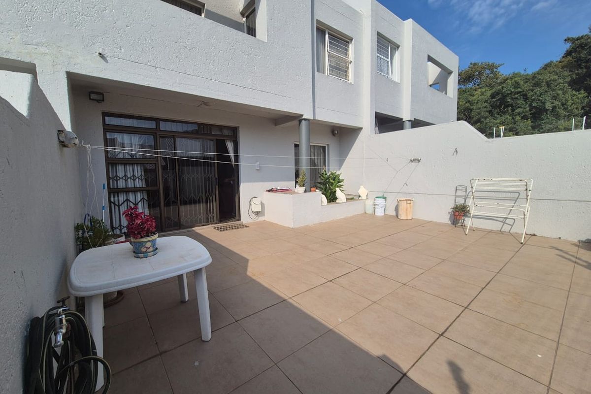 A spacious paved rear patio area featuring sliding door access to the townhouse interior and a private enclosed courtyard setting.