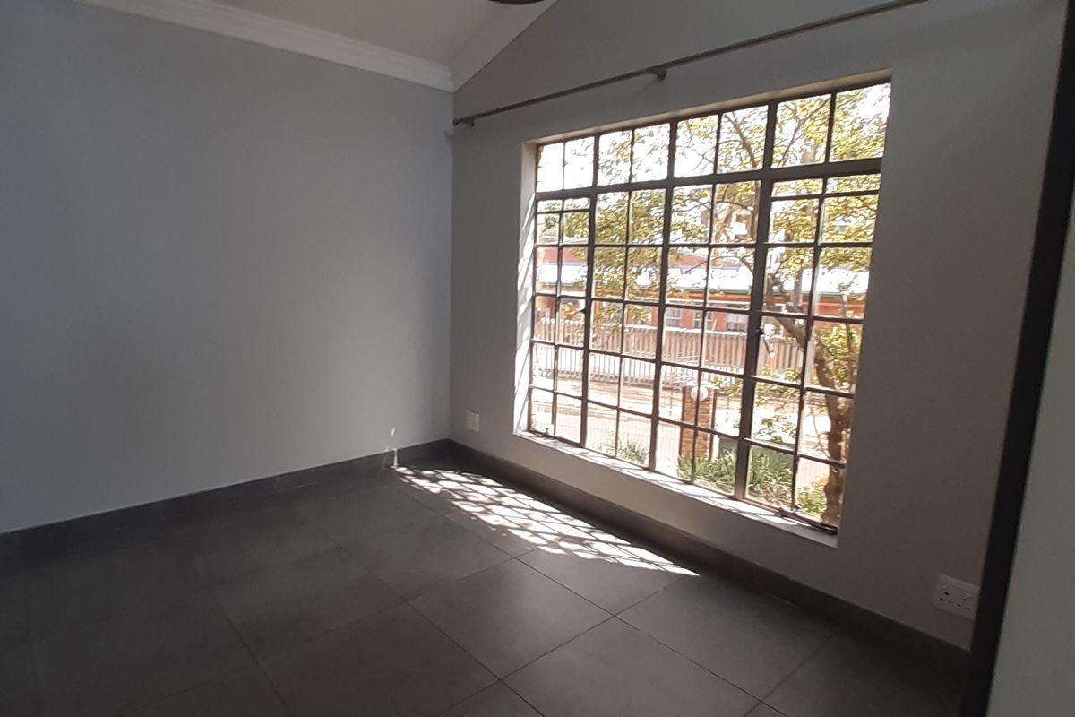 A bright, empty bedroom featuring large grid-pattern windows, neutral wall tones, and dark tiled flooring, offering a clean canvas for personalization.