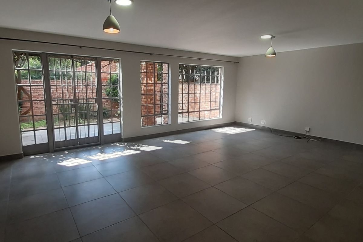Spacious, empty living room featuring large windows, tiled flooring, and a glass sliding door providing access to the outdoor area.