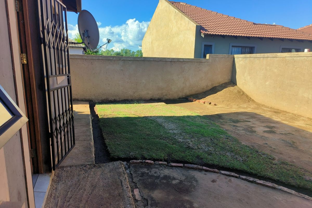 A rear exterior view of the property featuring a small patch of lawn, concrete paving, and perimeter boundary walls.