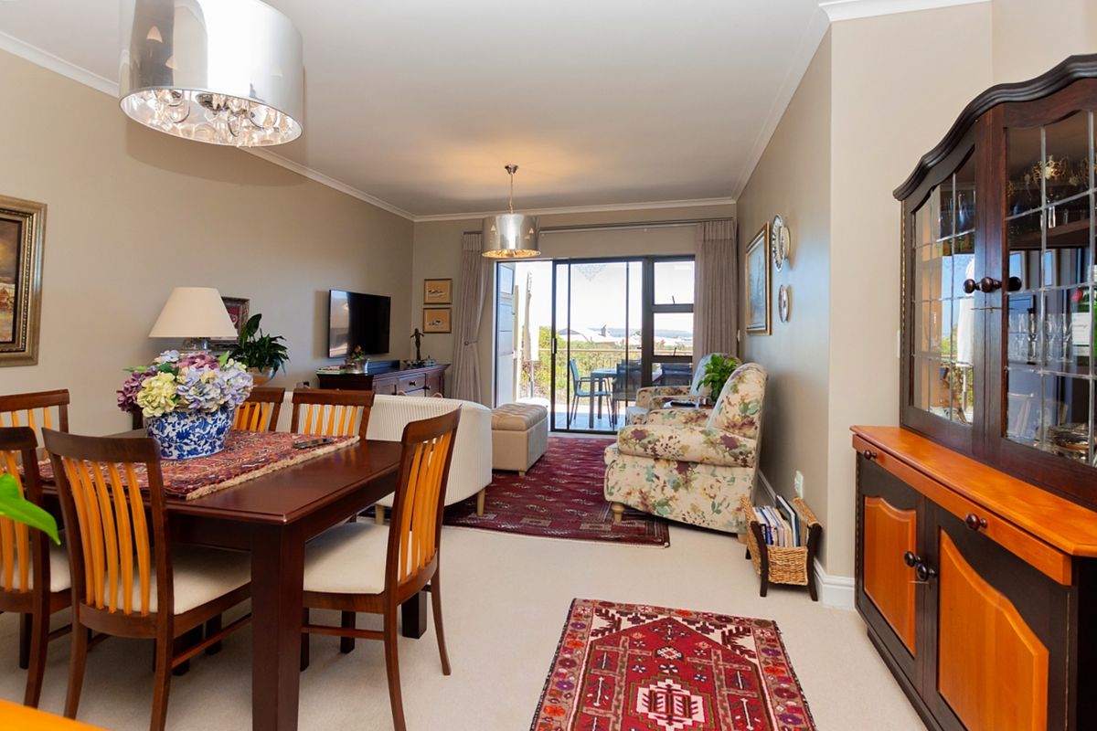 An open-plan living and dining area featuring neutral wall tones, carpeted flooring, and a sliding glass door leading to an outdoor balcony.