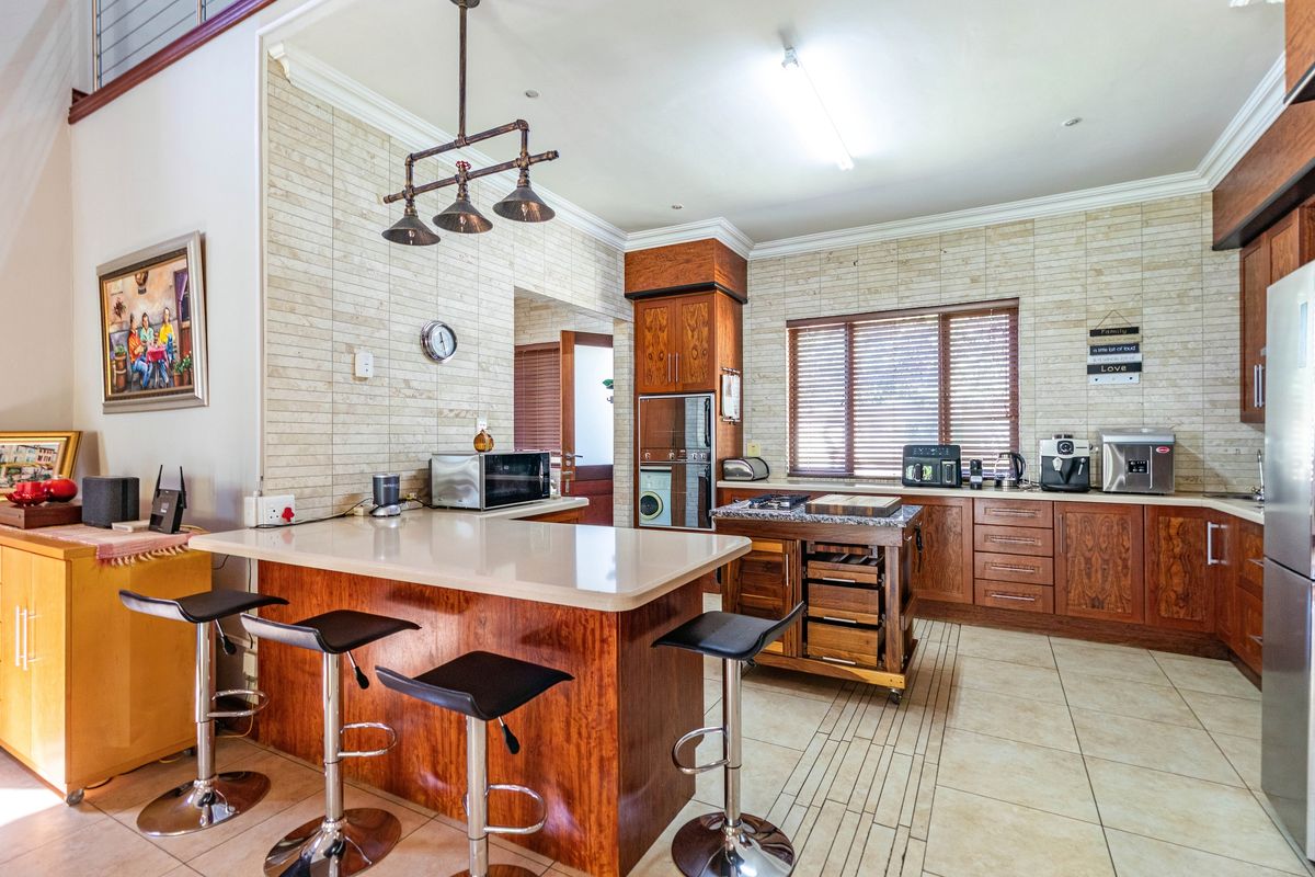 Spacious kitchen featuring wooden cabinetry, a central island with breakfast bar seating, stone-look wall tiling, and integrated storage solutions.