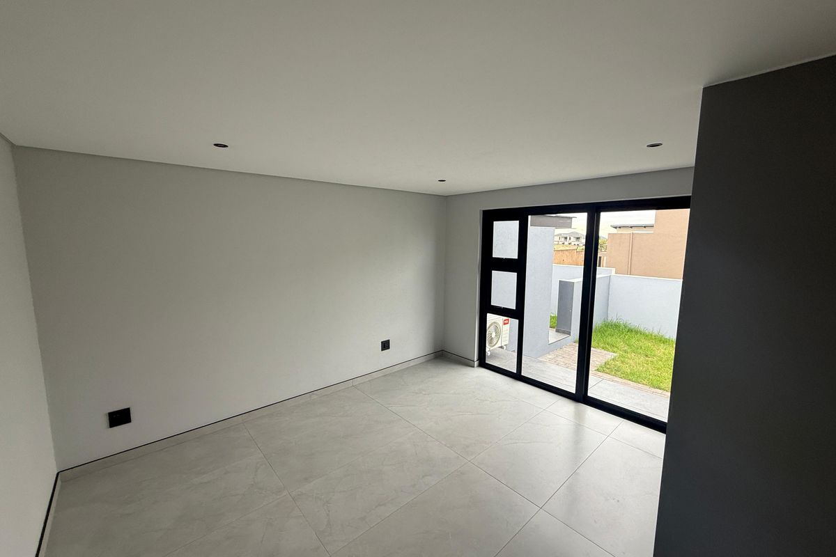 A bright, modern, and empty bedroom featuring large sliding glass doors that provide direct access to a private outdoor garden area.