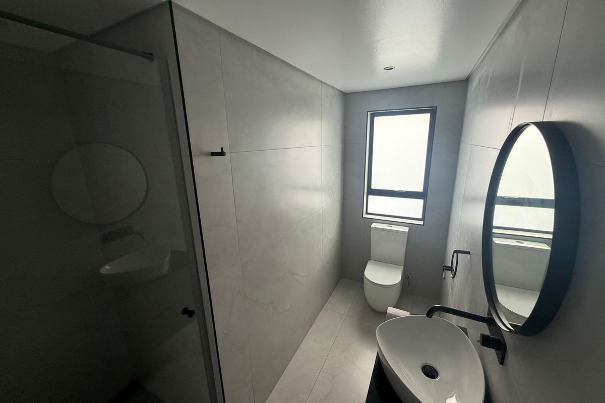 Modern bathroom featuring large-format grey wall and floor tiles, a sleek vessel sink with matte black fixtures, and a glass-enclosed shower.