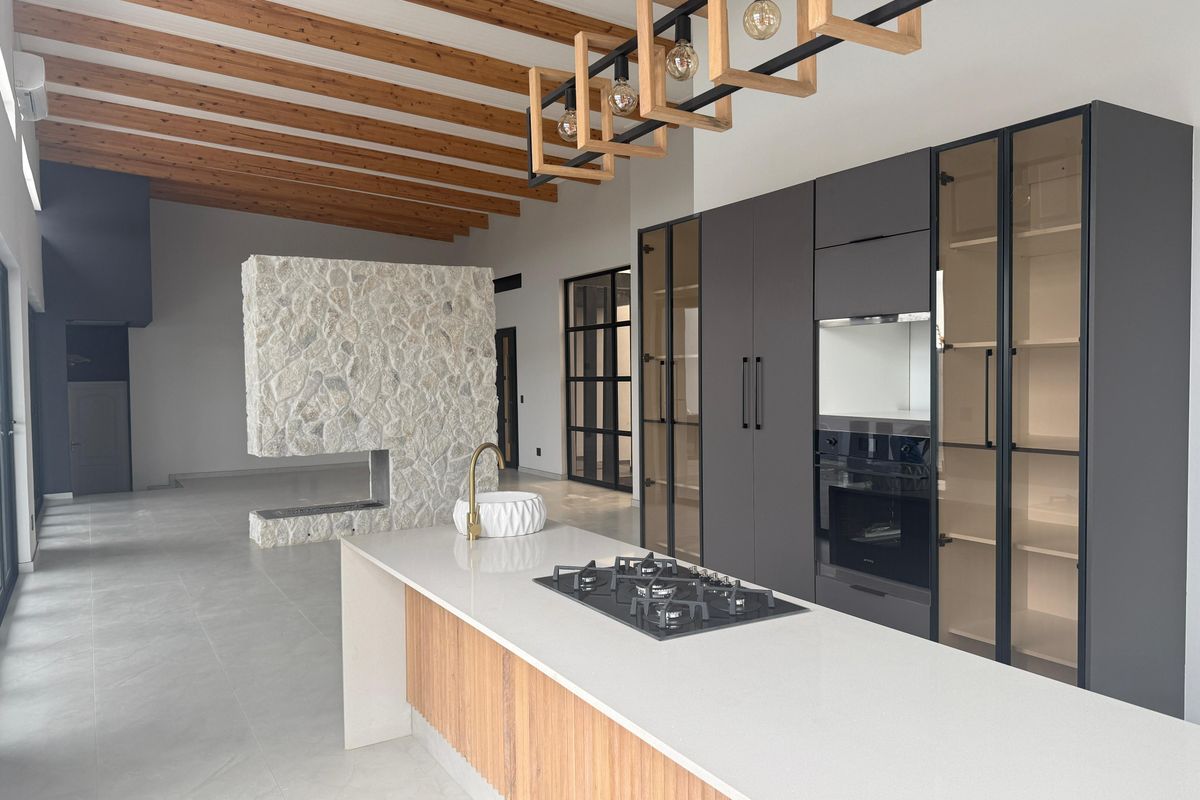 Modern open-plan kitchen featuring a central island with gas hob, sleek dark cabinetry, integrated oven, and a striking stone-clad fireplace feature.