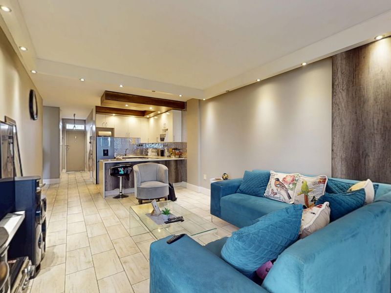 An open-plan living and kitchen area featuring tiled flooring, recessed lighting, and a modern kitchen with a breakfast island and timber ceiling accents.