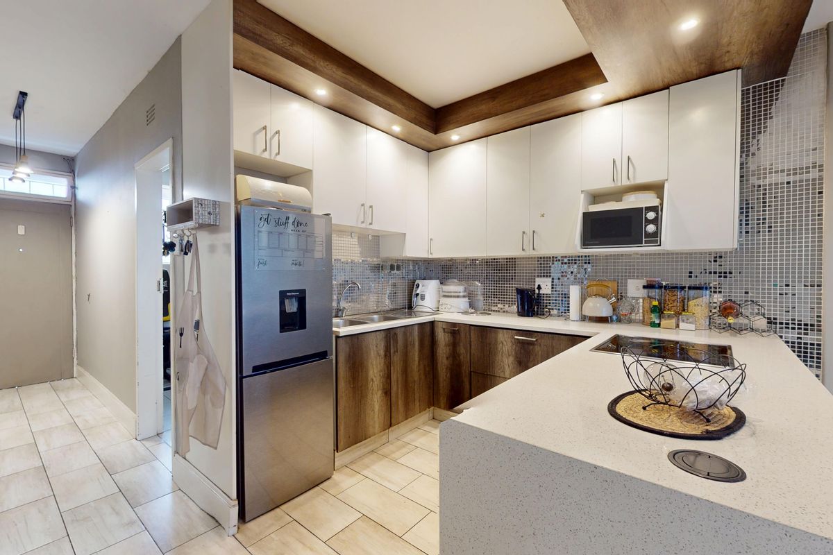 Modern kitchen featuring two-tone cabinetry, stone countertops, mosaic tile backsplash, and integrated appliances, seamlessly flowing into the adjacent living area.