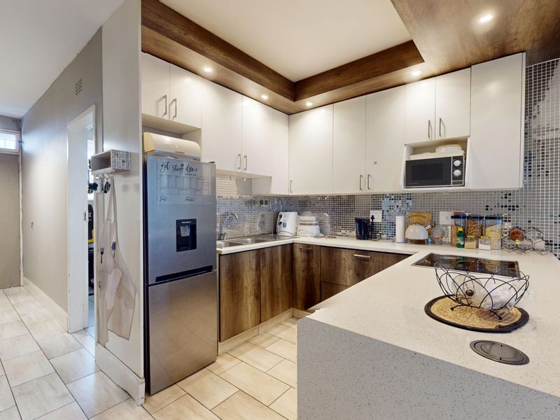 Modern kitchen featuring two-tone cabinetry, stone countertops, mosaic tile backsplash, and integrated appliances, seamlessly flowing into the adjacent living area.