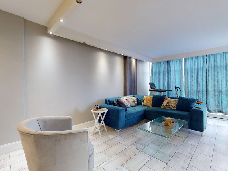 A bright living room featuring tiled flooring, recessed ceiling lighting, and large windows allowing for ample natural light.