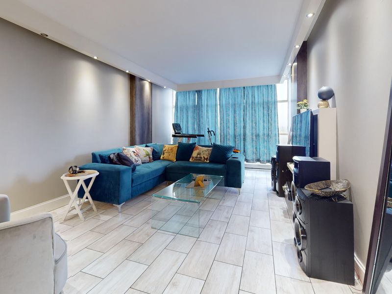 A well-lit living room featuring modern tiled flooring and recessed ceiling lights, offering a comfortable and bright space.