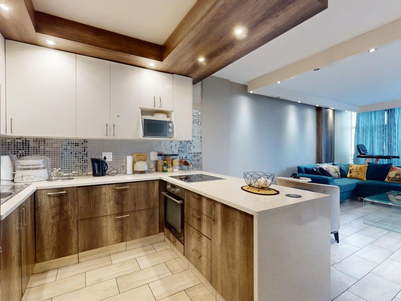 Modern open-plan kitchen featuring two-tone cabinetry, stone countertops, mosaic backsplash, and integrated appliances, flowing seamlessly into the adjacent living area.