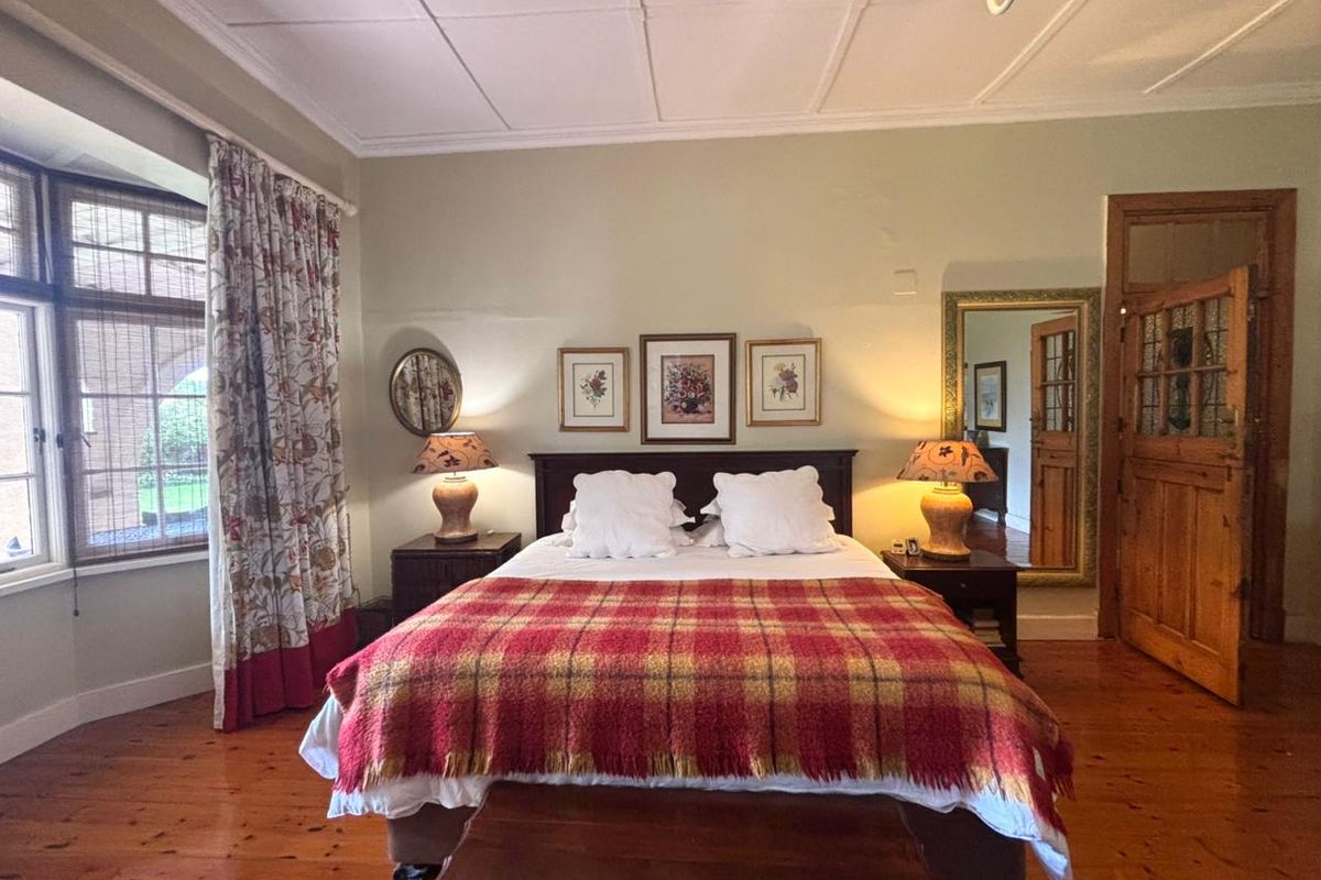 A spacious bedroom featuring polished timber flooring, a classic bay window, and traditional wooden door detailing, offering a warm and inviting atmosphere.