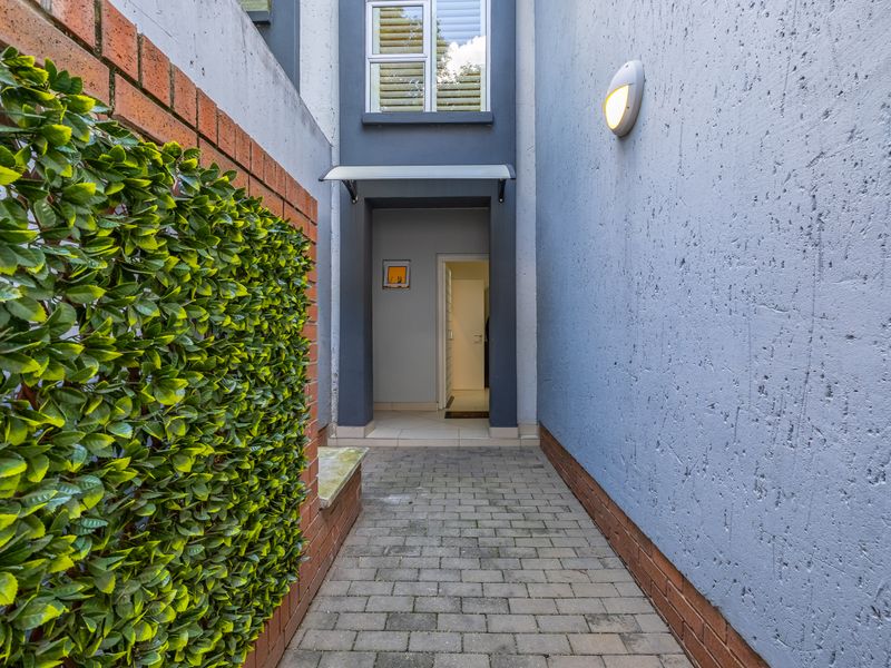 A paved entrance walkway leading to the front door, featuring a brick boundary wall and modern exterior lighting.