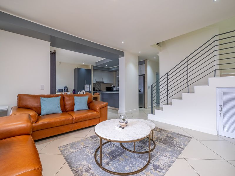 Spacious open-plan living area featuring tiled floors, a modern staircase with metal railings, and a seamless transition into the kitchen space.