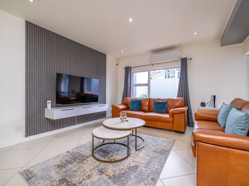 Modern living room featuring stylish slatted acoustic wall paneling, a floating media console, tiled flooring, and a wall-mounted air conditioning unit.