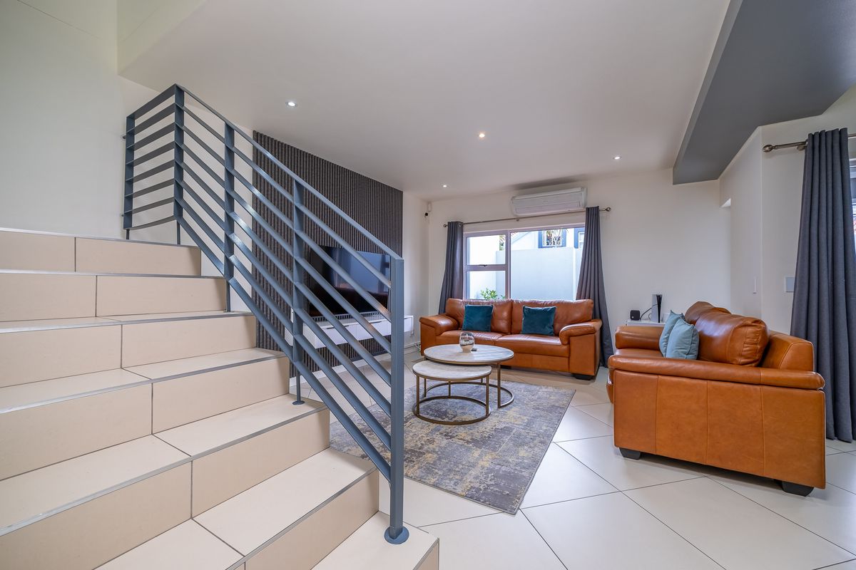 Modern living room featuring tiled flooring, a contemporary staircase with metal balustrade, a slatted feature wall, and a split-system air conditioner.