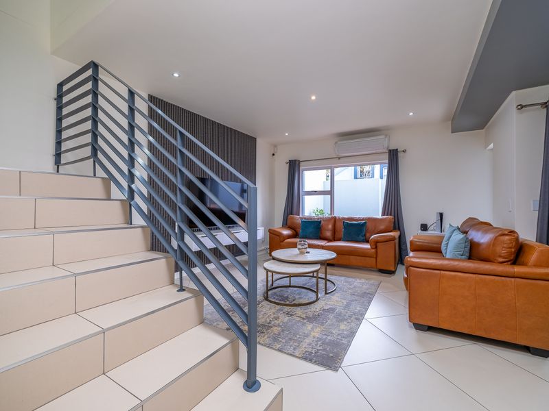 Modern living room featuring tiled flooring, a contemporary staircase with metal balustrade, a slatted feature wall, and a split-system air conditioner.