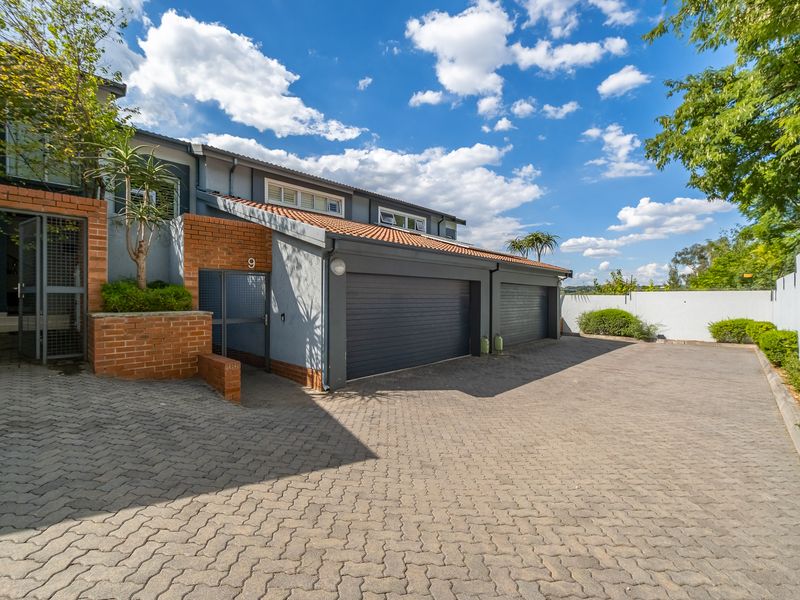 Front exterior view of a townhouse featuring a double garage, paved driveway, and brick accents under a tiled roof.