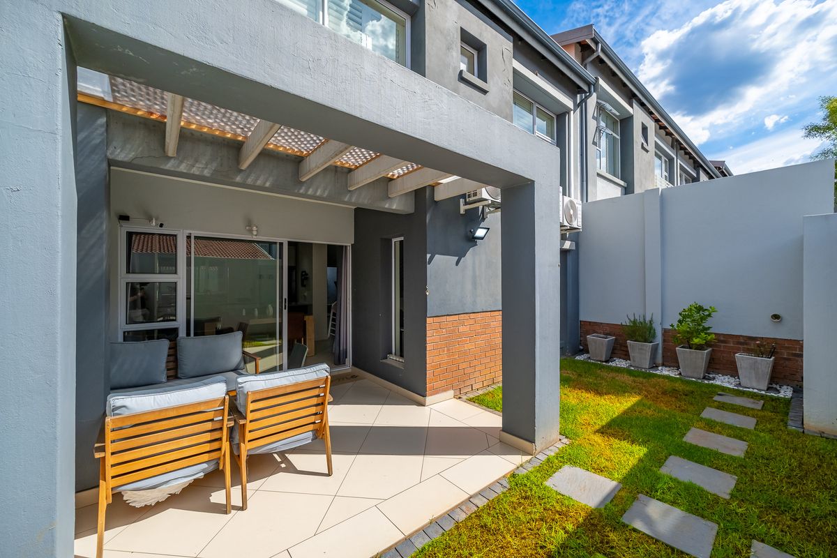 A well-maintained rear townhouse exterior featuring a covered patio with a pergola, sliding door access, and a private garden with a paved walkway.