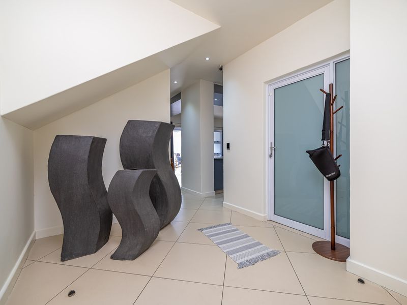 A bright and modern entrance hall featuring neutral tiled flooring, recessed lighting, and a contemporary frosted glass front door.