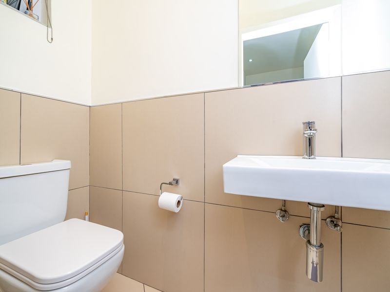 A clean and modern guest bathroom featuring a wall-mounted basin, chrome fixtures, and neutral ceramic wall tiling.
