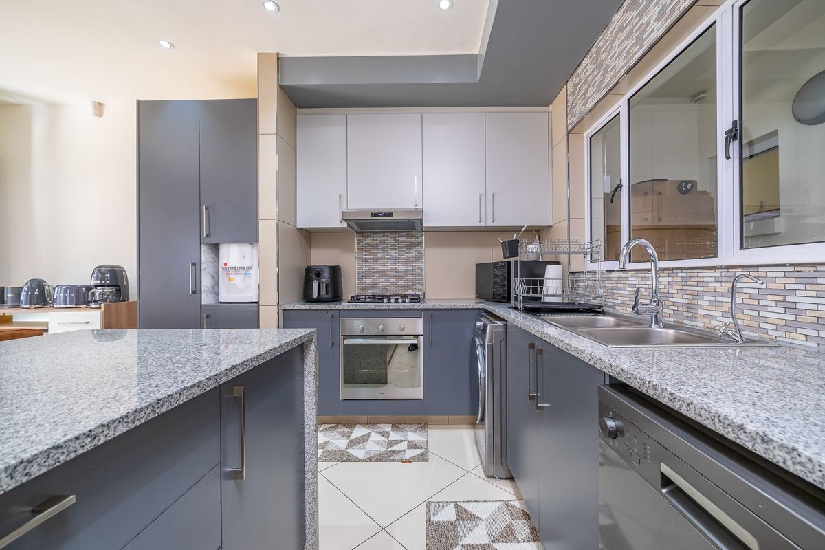 Modern kitchen featuring granite countertops, built-in oven, gas hob, extractor fan, and ample cabinetry with a stylish mosaic tile backsplash.